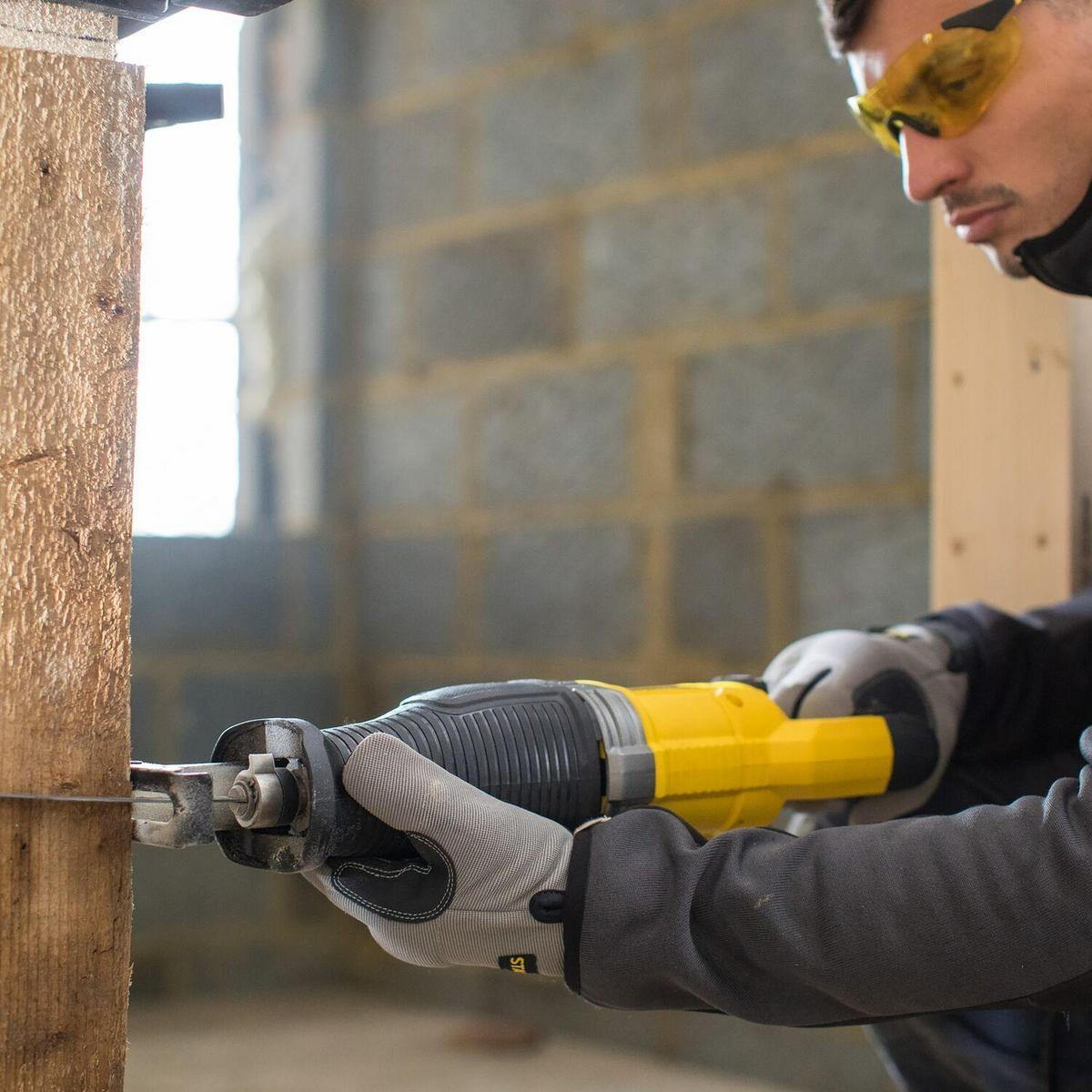 Man wearing goggles saws wood with a yellow reciprocating saw.