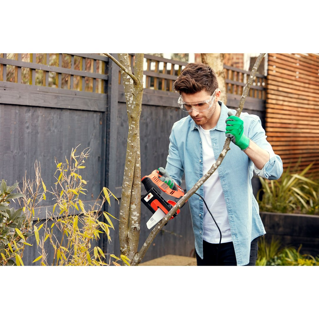 Mężczyzna w goglach i rękawicach tnie gałąź piłą.