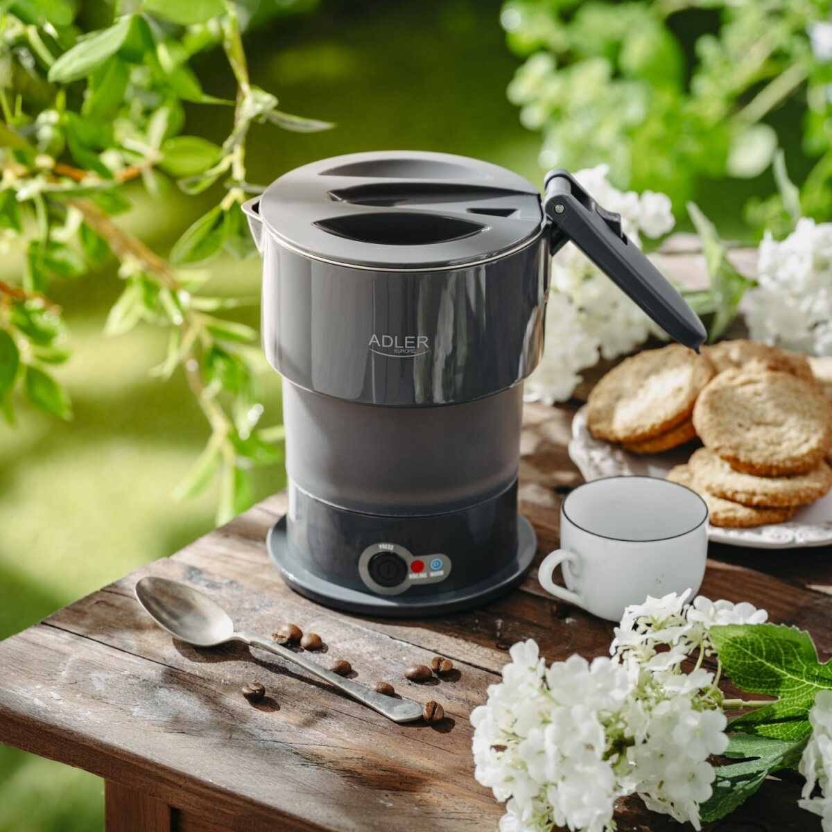 Szara czajnik stoi na drewnianym stole z ciastkami, filiżanką i ziarnami kawy.