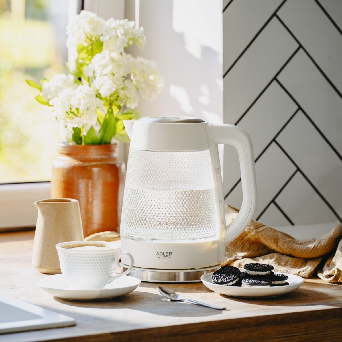 Ein weißer Wasserkocher mit Wasser, daneben eine Tasse Kaffee und Kekse.