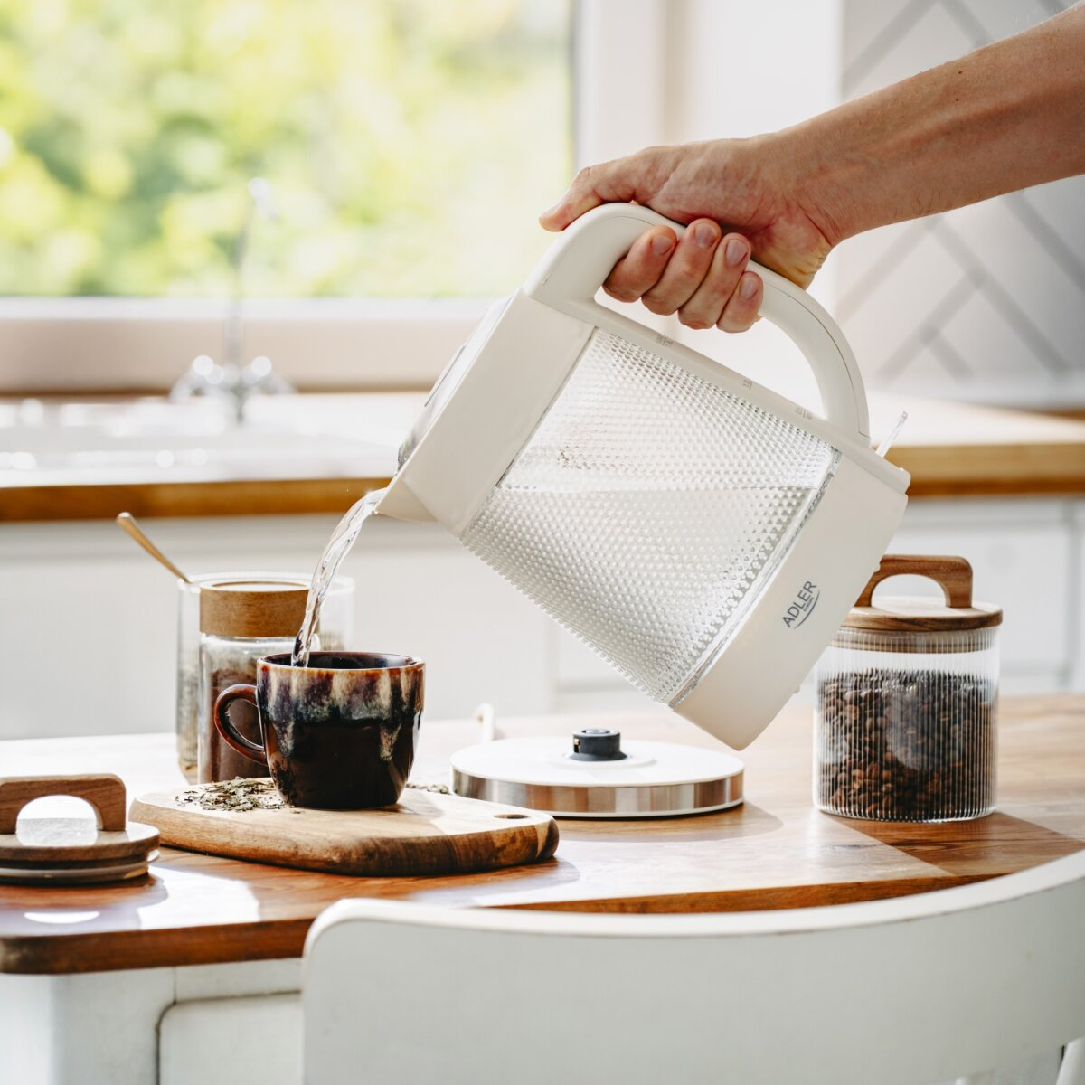 Wasser wird aus einem weißen Wasserkocher in eine dunkle Tasse gegossen.