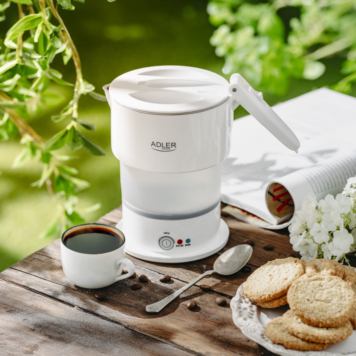 Ein weißer Wasserkocher steht auf einem Holztisch mit Kaffee, Keksen und einem Löffel.