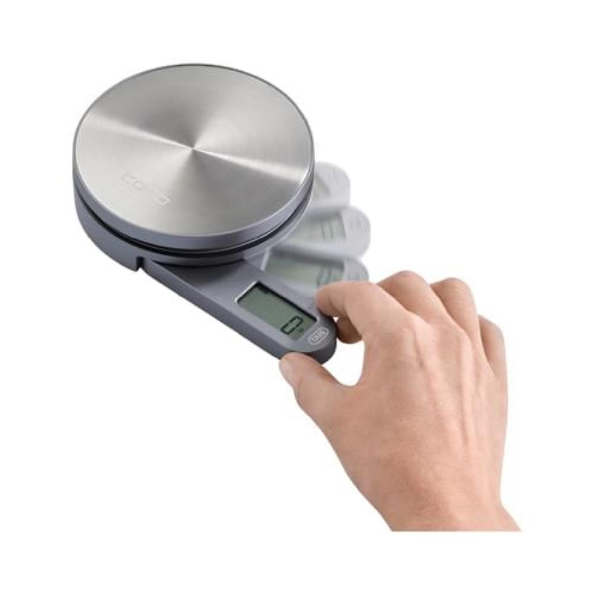 Eine Hand drückt die Tara-Taste einer digitalen Küchenwaage mit silberner Oberseite.