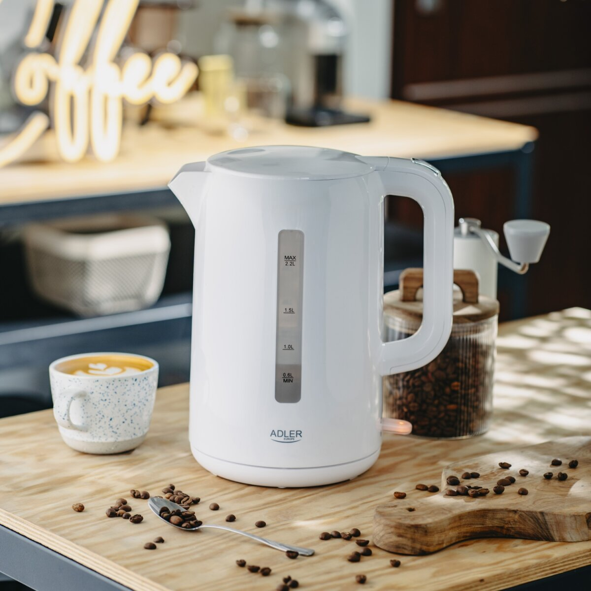 Ein weißer Wasserkocher steht auf einem Holztisch neben einer Tasse Kaffee und Kaffeebohnen.
