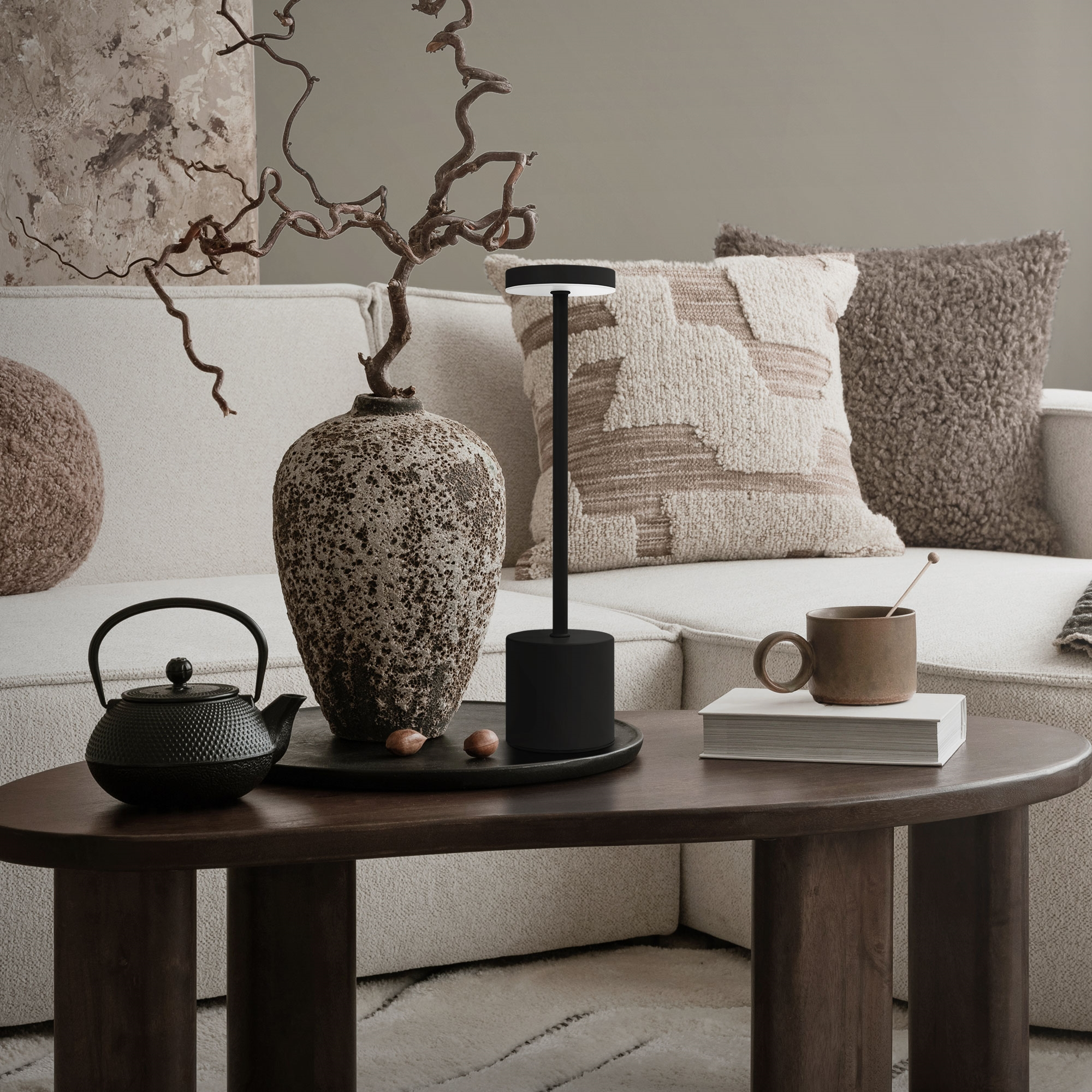 Ein Couchtisch mit Vase, Lampe, Teekanne, Tasse und Buch vor einem Sofa.