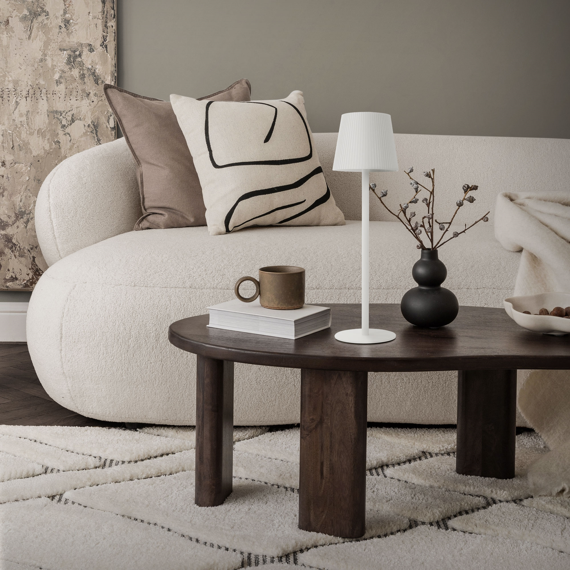Ein beiger Bouclé-Sofa mit Kissen, ein Couchtisch mit Lampe, Vase und Buch.