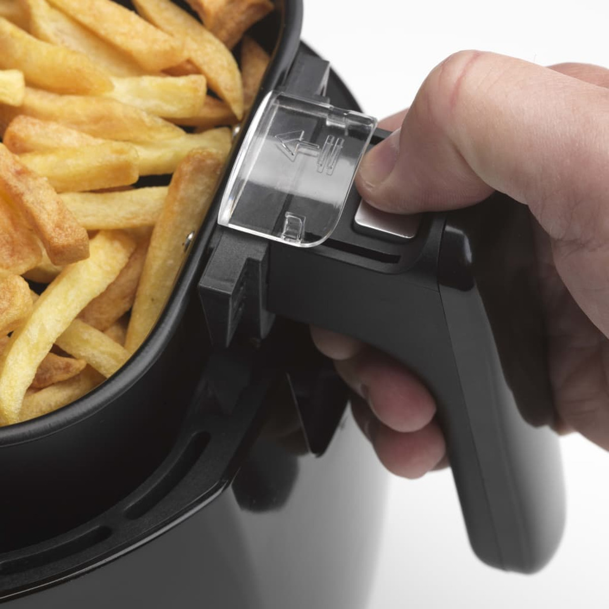 Una mano afferra il manico di un cestello nero per friggitrice ad aria pieno di patatine fritte dorate.