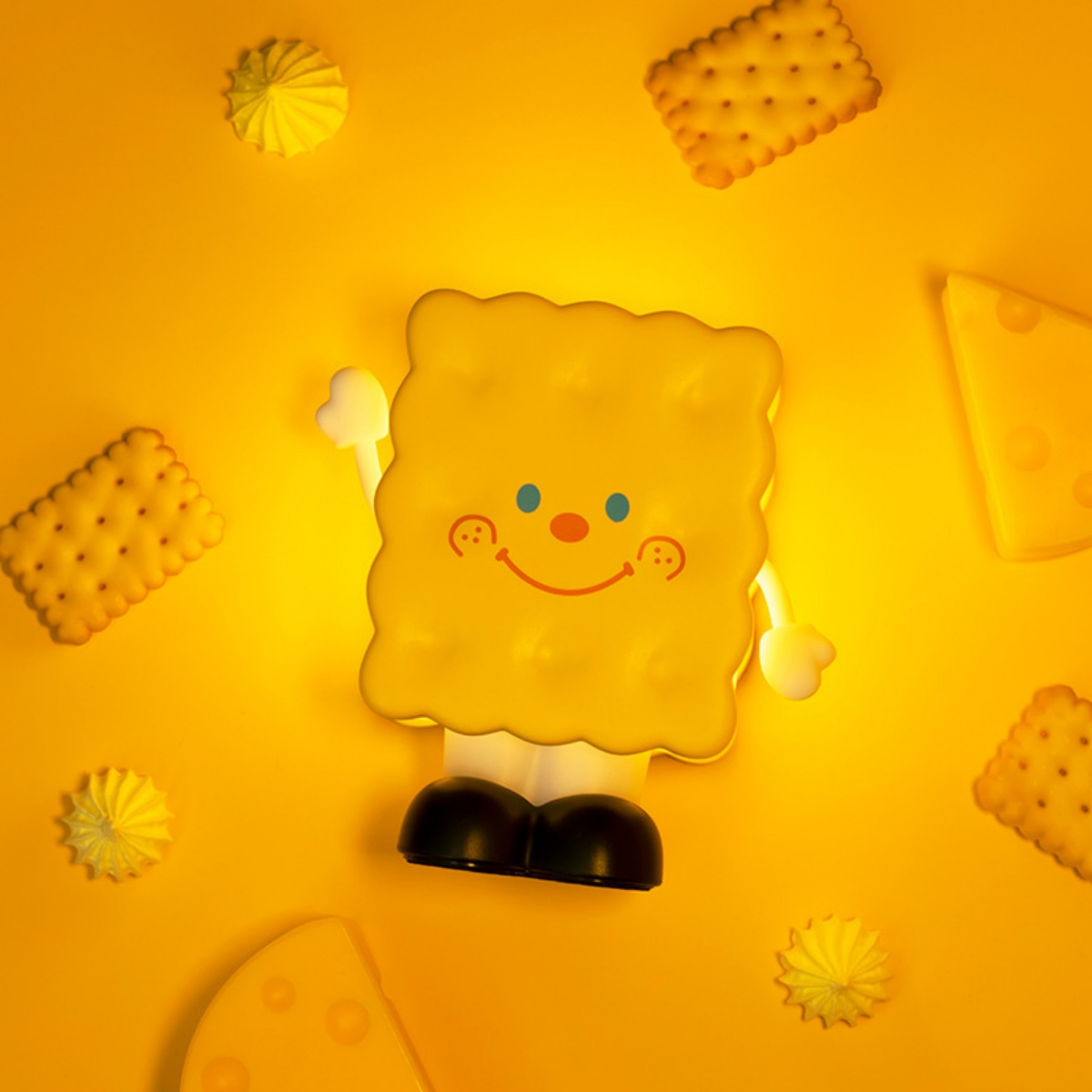 Eine gelbe Kekz-Lampe mit Gesicht, umgeben von weiteren Keksen und Käsestücken.