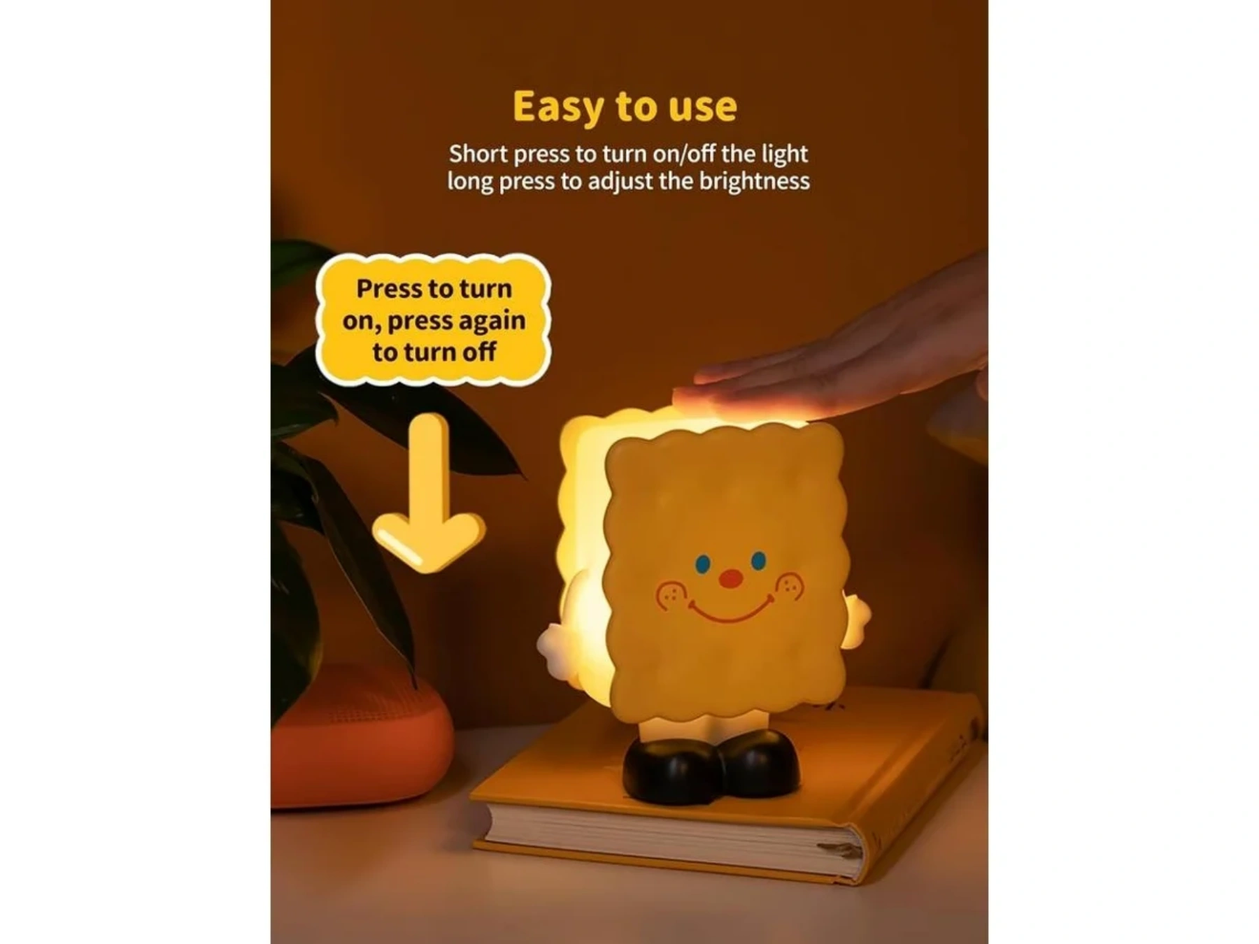 Eine gelbe Kekslampe mit Gesicht steht auf einem Buch. Eine Hand berührt sie.