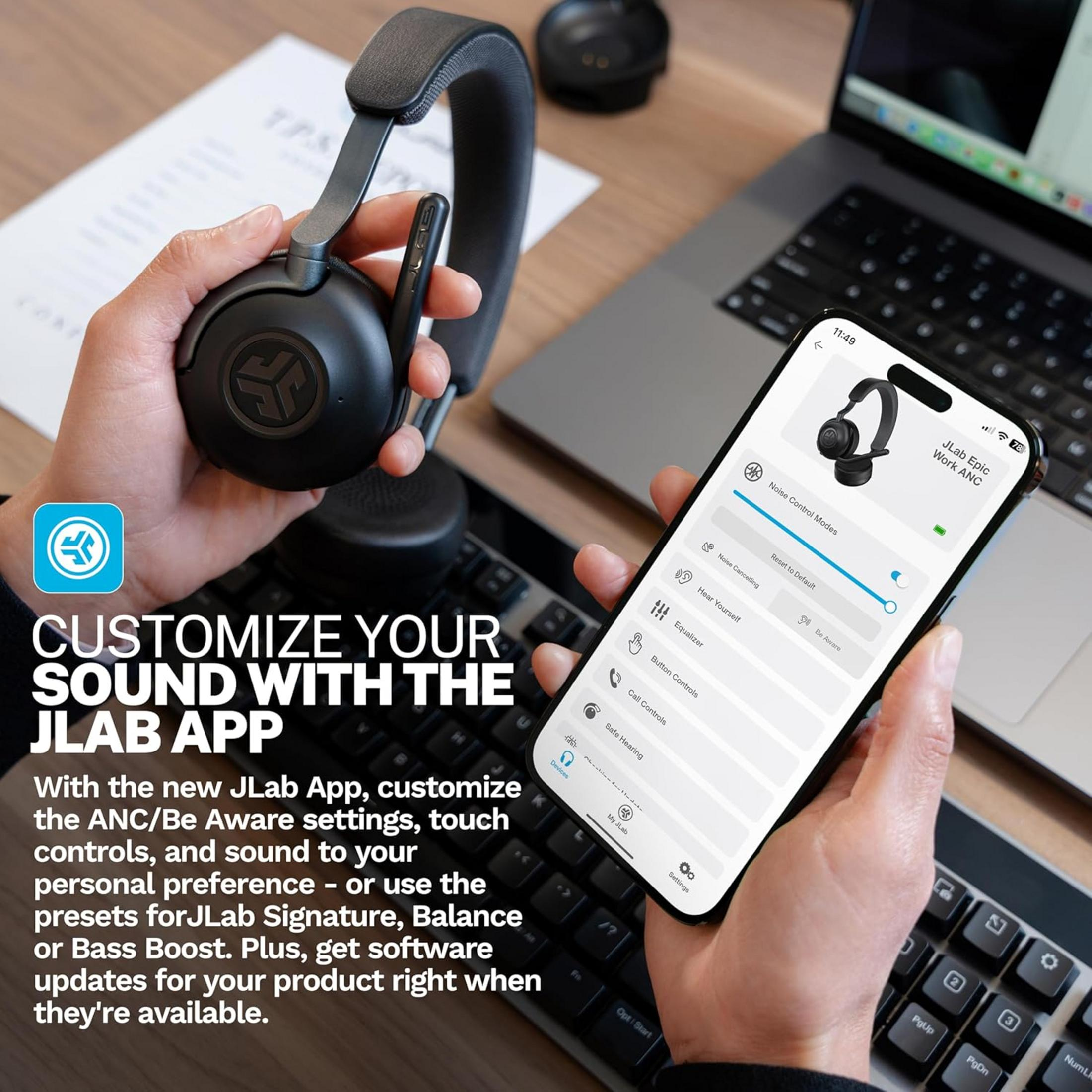 Persona tiene cuffie e smartphone con app JLab, laptop sullo sfondo.