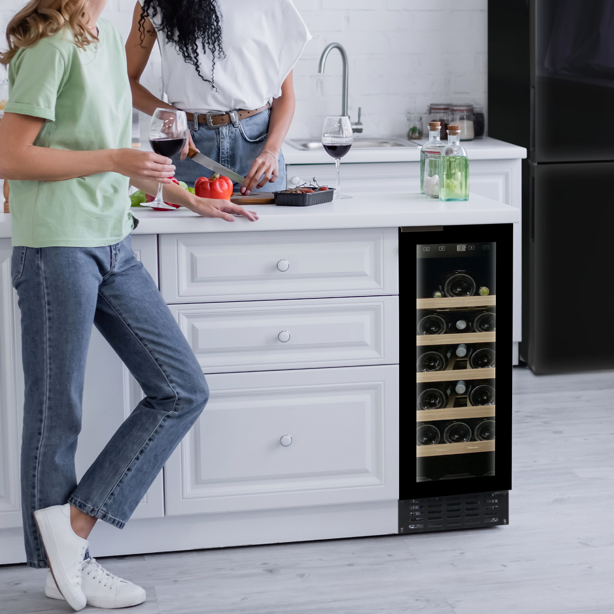 Dos mujeres en una cocina con vino; una corta pimiento, junto a un enfriador de vino.