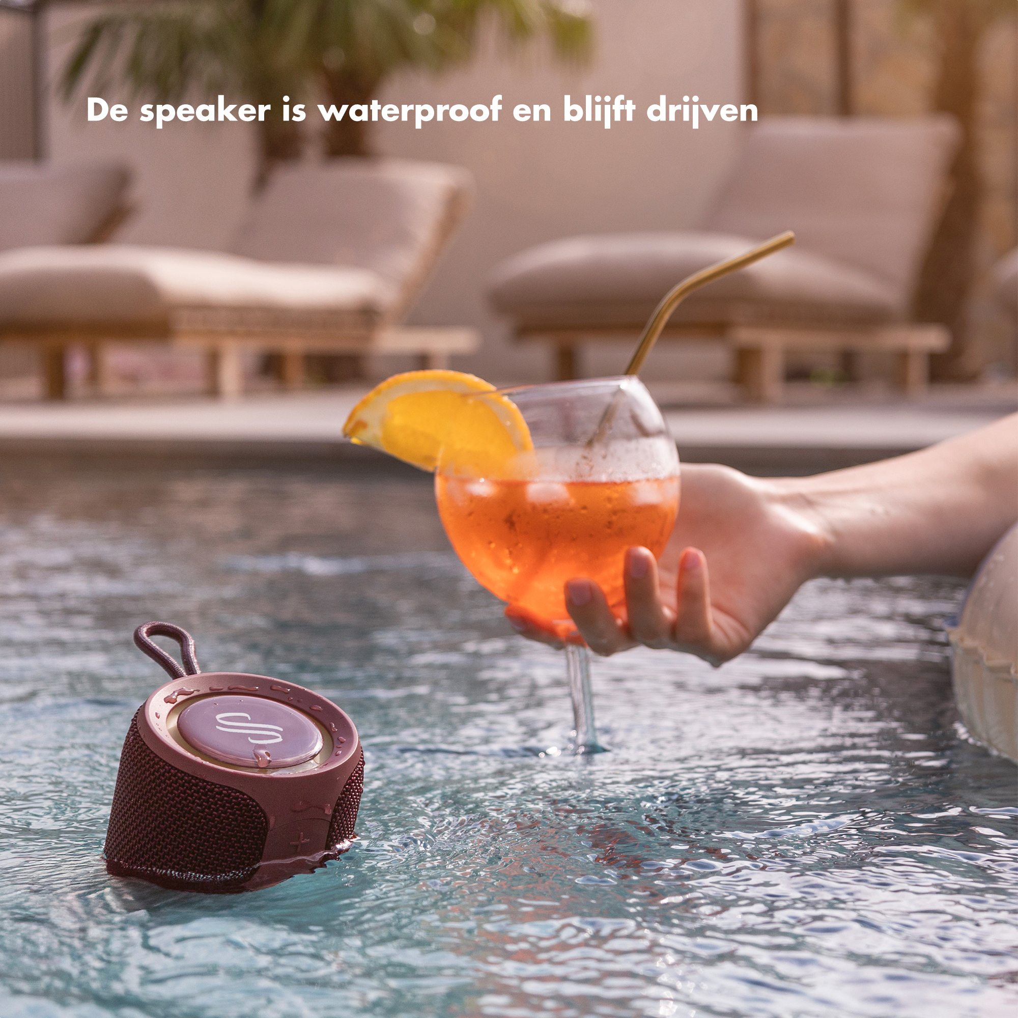 Een waterdichte luidspreker drijft in een zwembad naast een drankje.