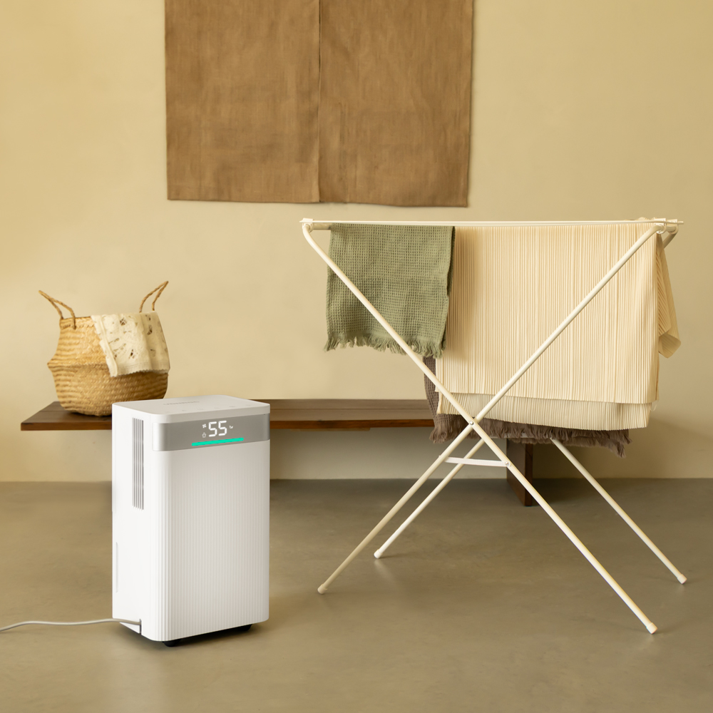 A white dehumidifier sits beside a drying rack with clothes on it.