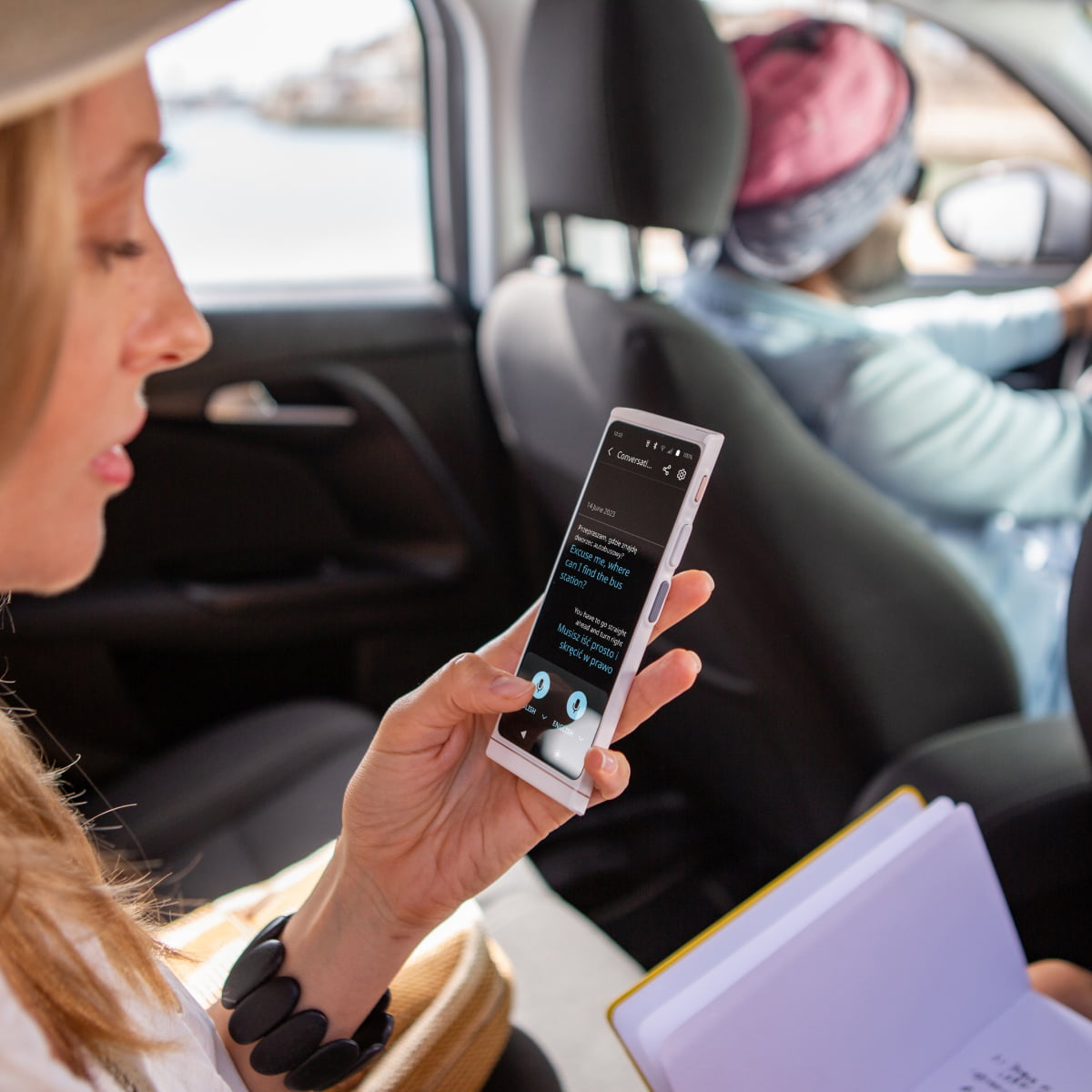 Eine Frau im Auto hält ein Smartphone, das eine Übersetzungs-App zeigt.