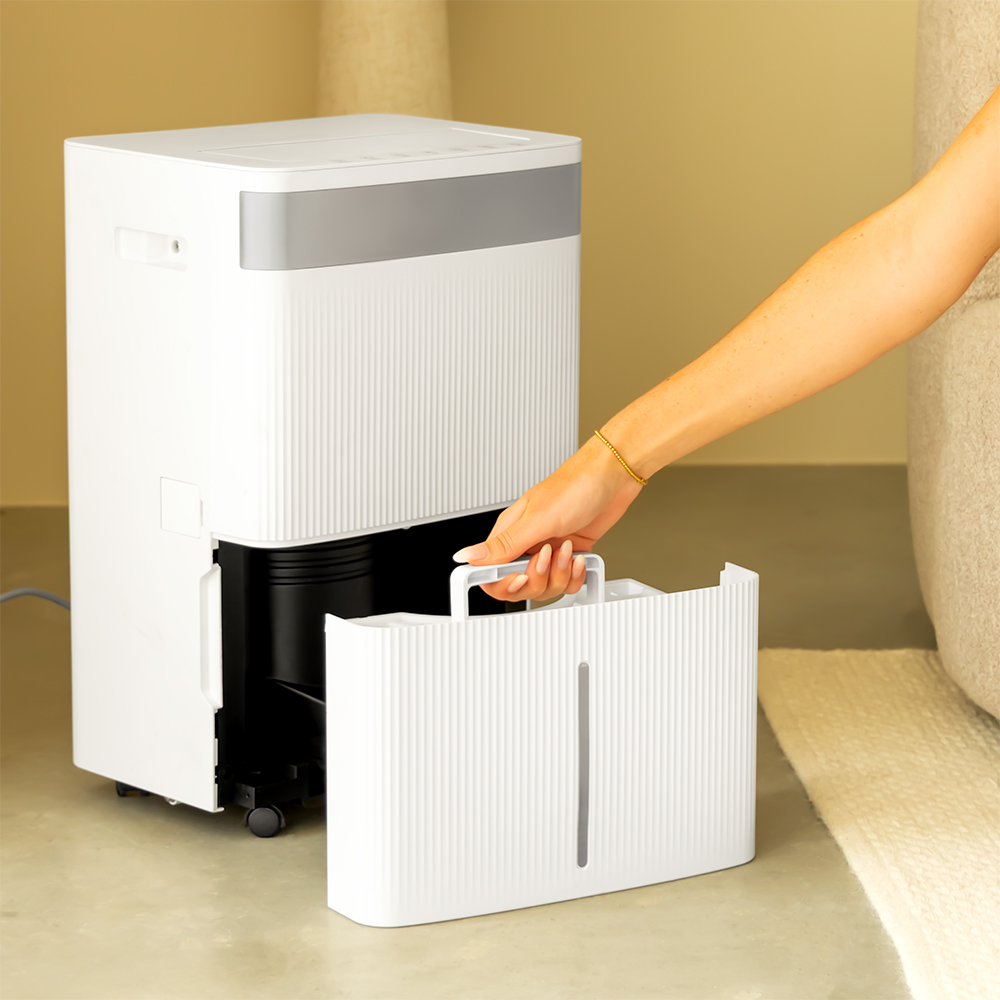 A hand removes a white water tank from a dehumidifier.