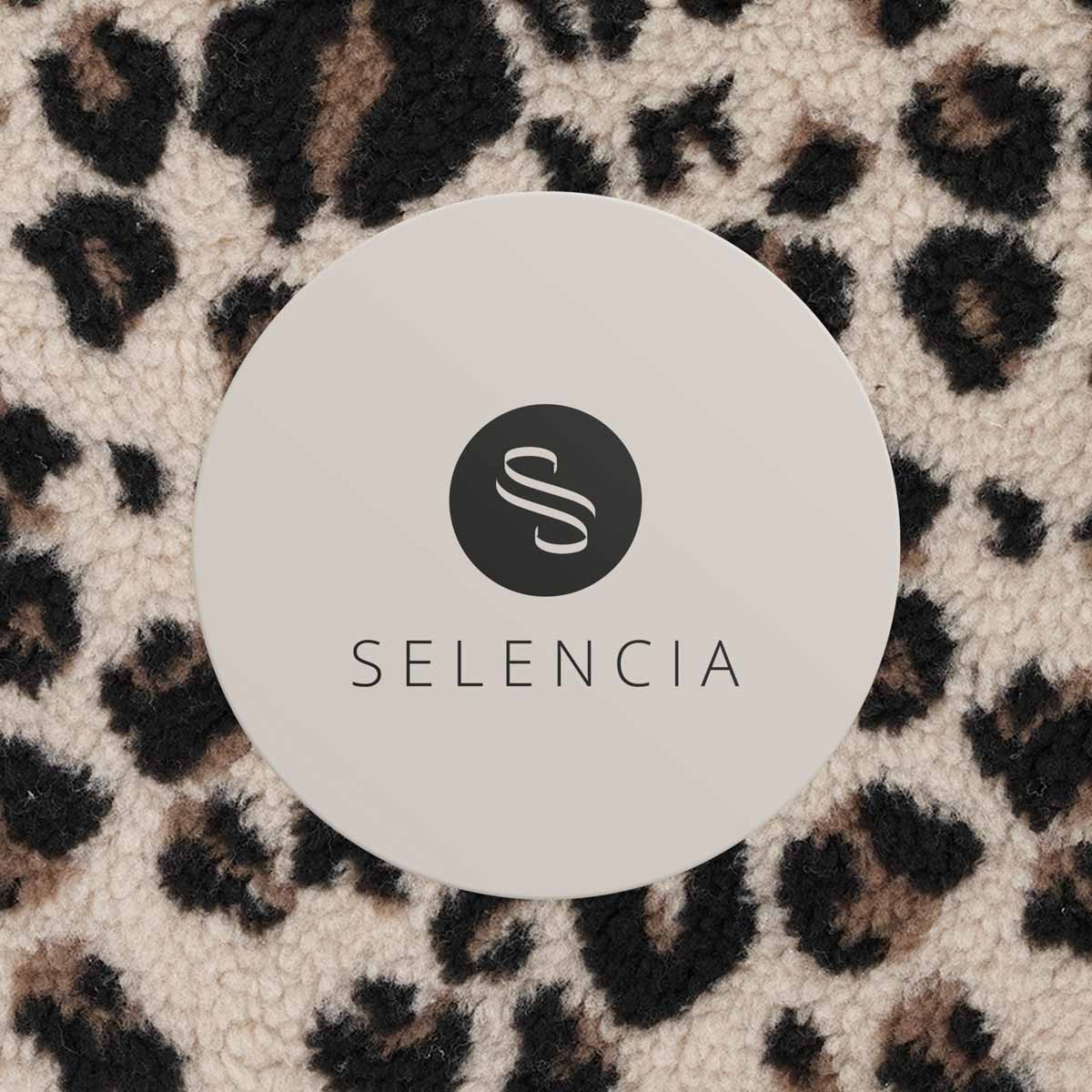 Una pegatina redonda con logo 'S' y texto 'SELENCIA' sobre estampado de leopardo.