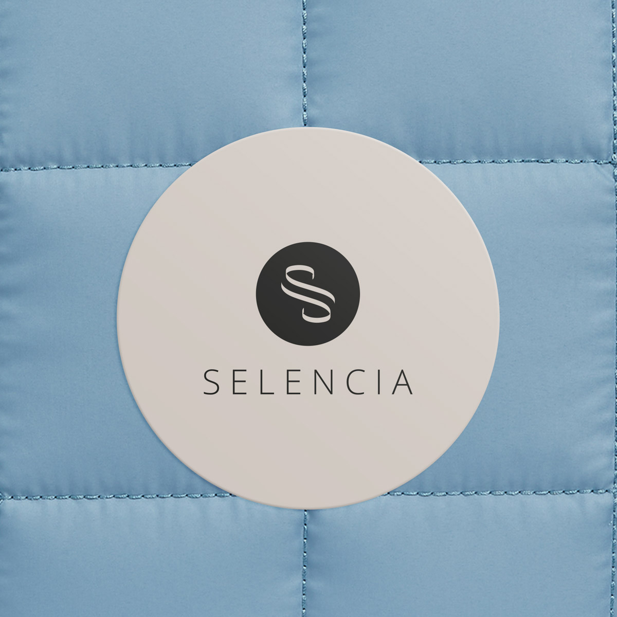 A circle with an S logo and the name SELENCIA on blue quilted fabric.
