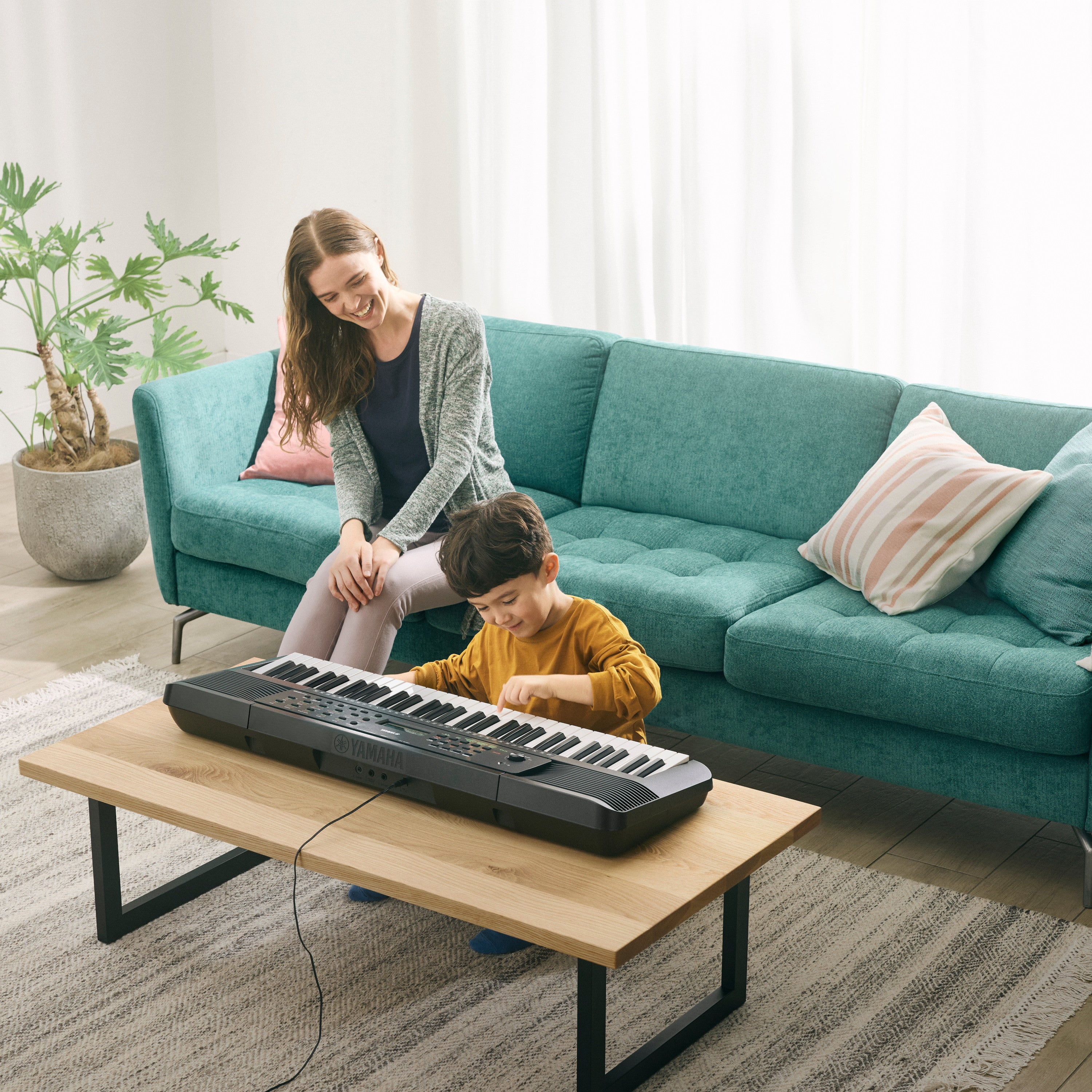 Ein Junge spielt auf einem Keyboard, eine Frau sitzt daneben auf dem Sofa.