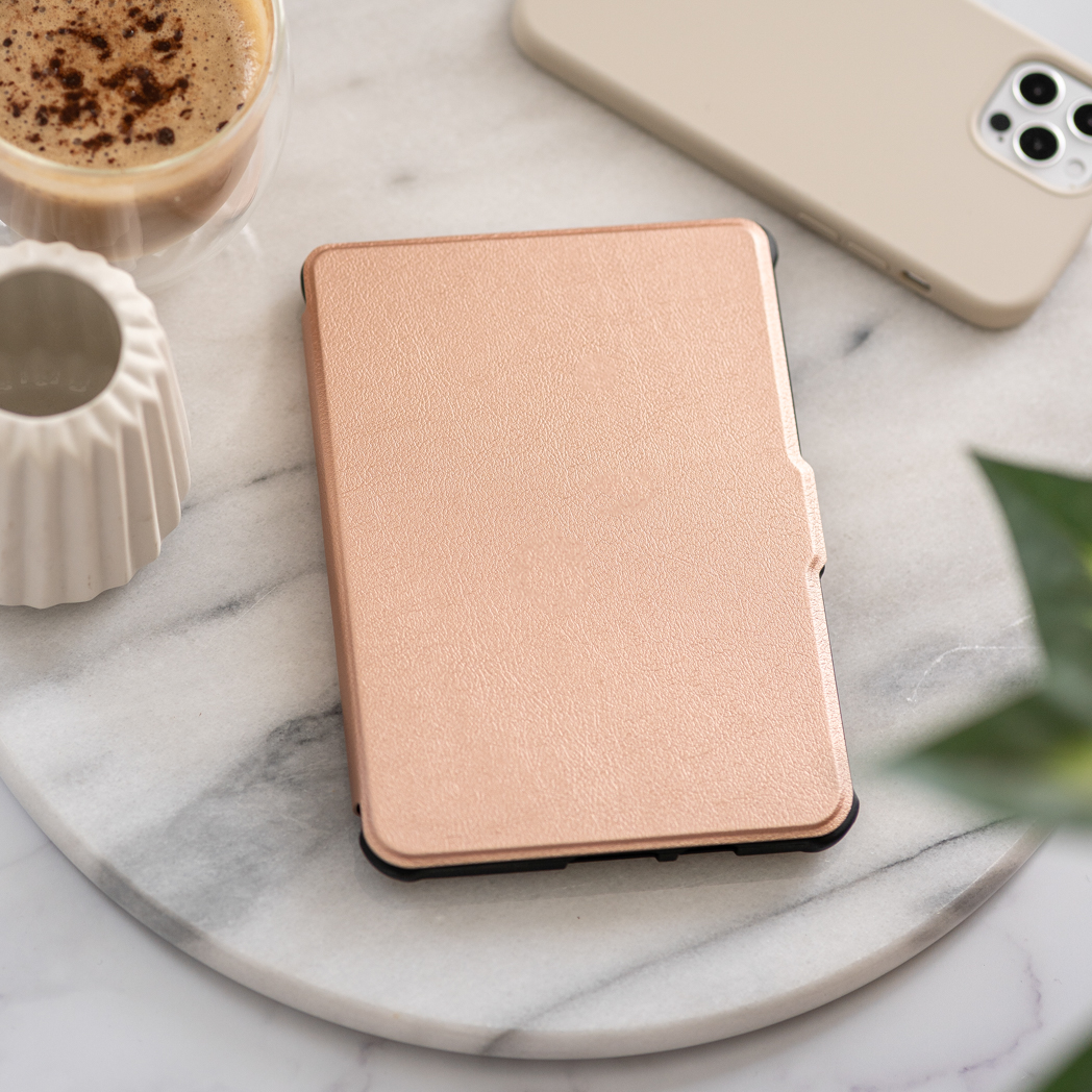 Un e-reader rose doré, avec un café et un téléphone à proximité.