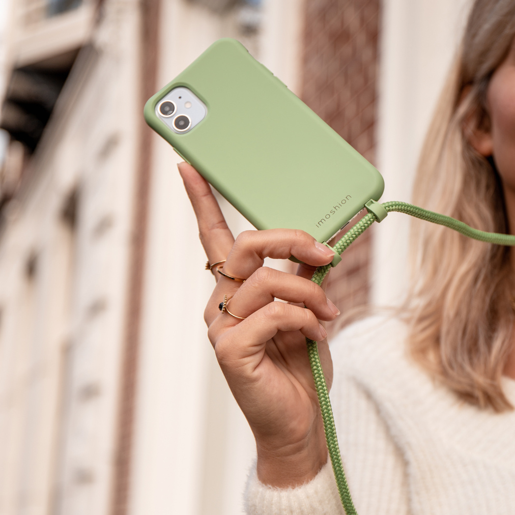 Een vrouw houdt een lichtgroene iPhone vast met een bijpassend koord.