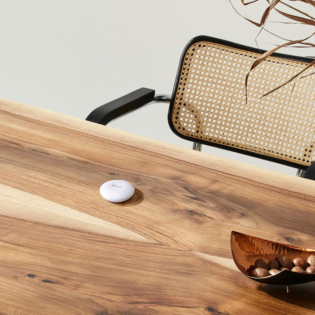 Biały czujnik na drewnianym stole obok miski z orzechami.