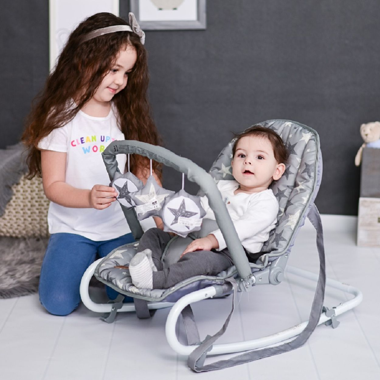 Ein kleines Mädchen kniet neben einem Baby in einem Schaukelstuhl mit Sternenmuster.