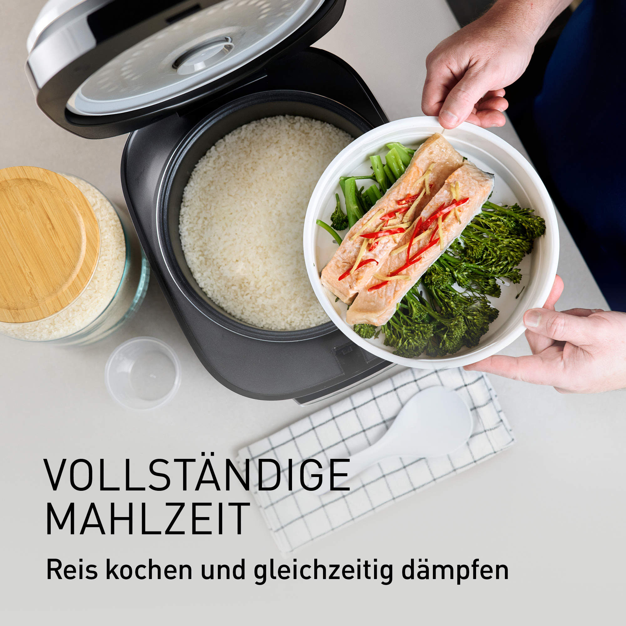 Reiskocher mit Reis, dampfendem Lachs und Brokkoli daneben.