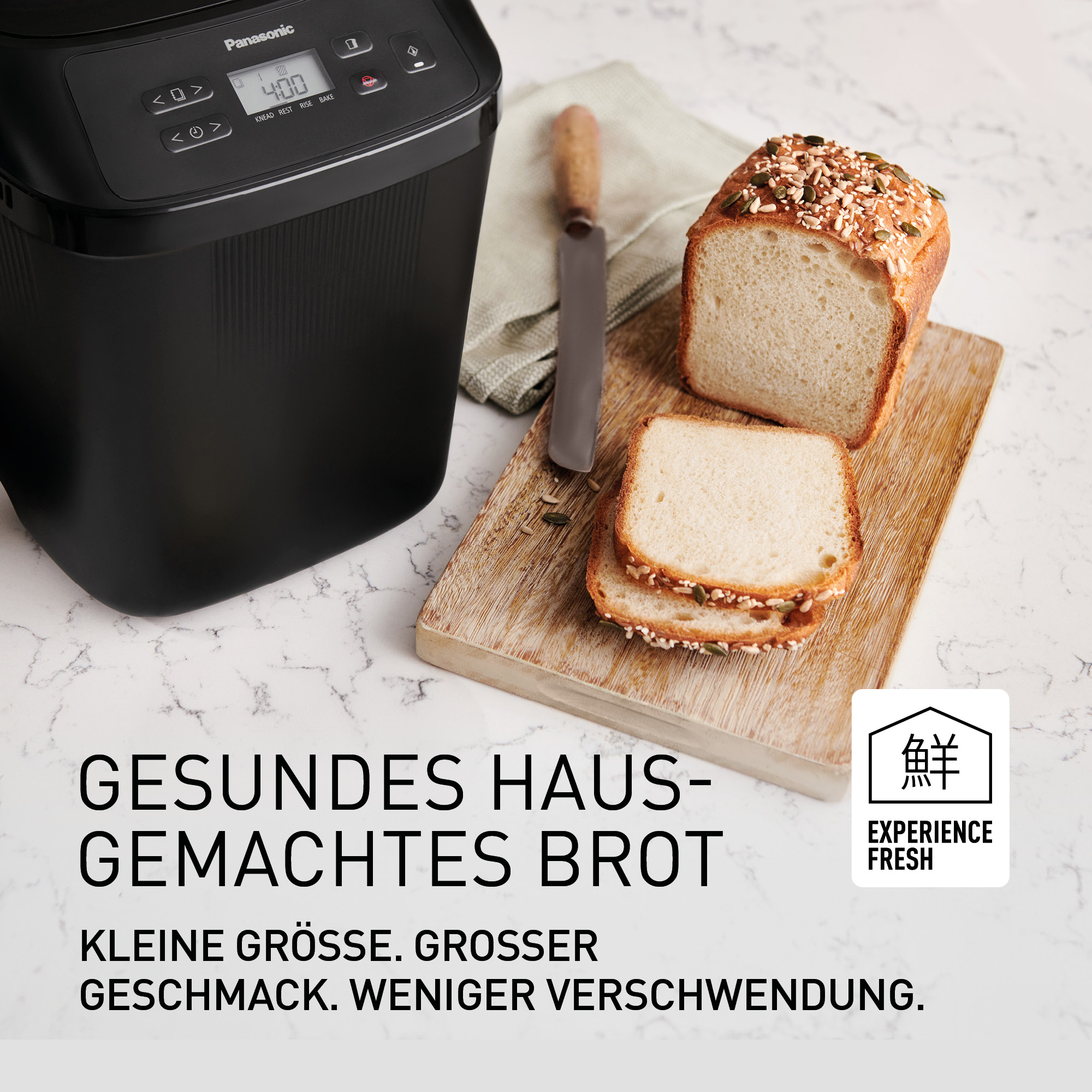 Ein schwarzer Brotbackautomat neben einem Holzbrett mit Brot.