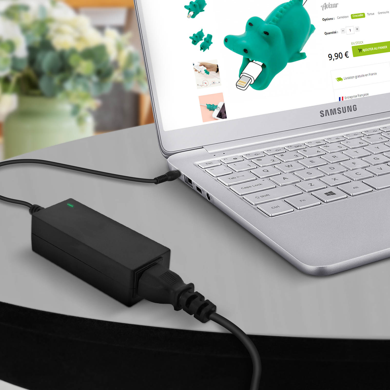 Un sujetacables de cocodrilo verde está conectado a un portátil, con un adaptador de corriente cerca.