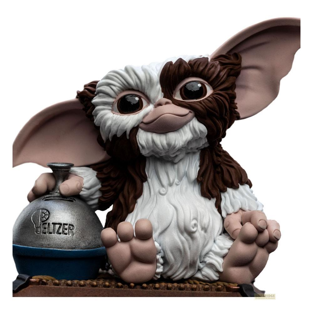 Gizmo sitzt und hält eine silberne Sprudelflasche mit blauer Basis.