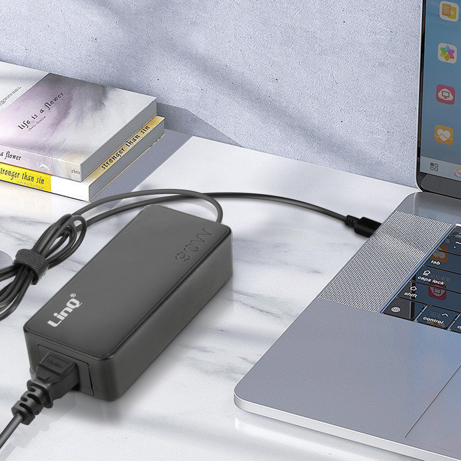 Ein schwarzes Netzteil ist an einen Laptop angeschlossen, daneben liegen Bücher.