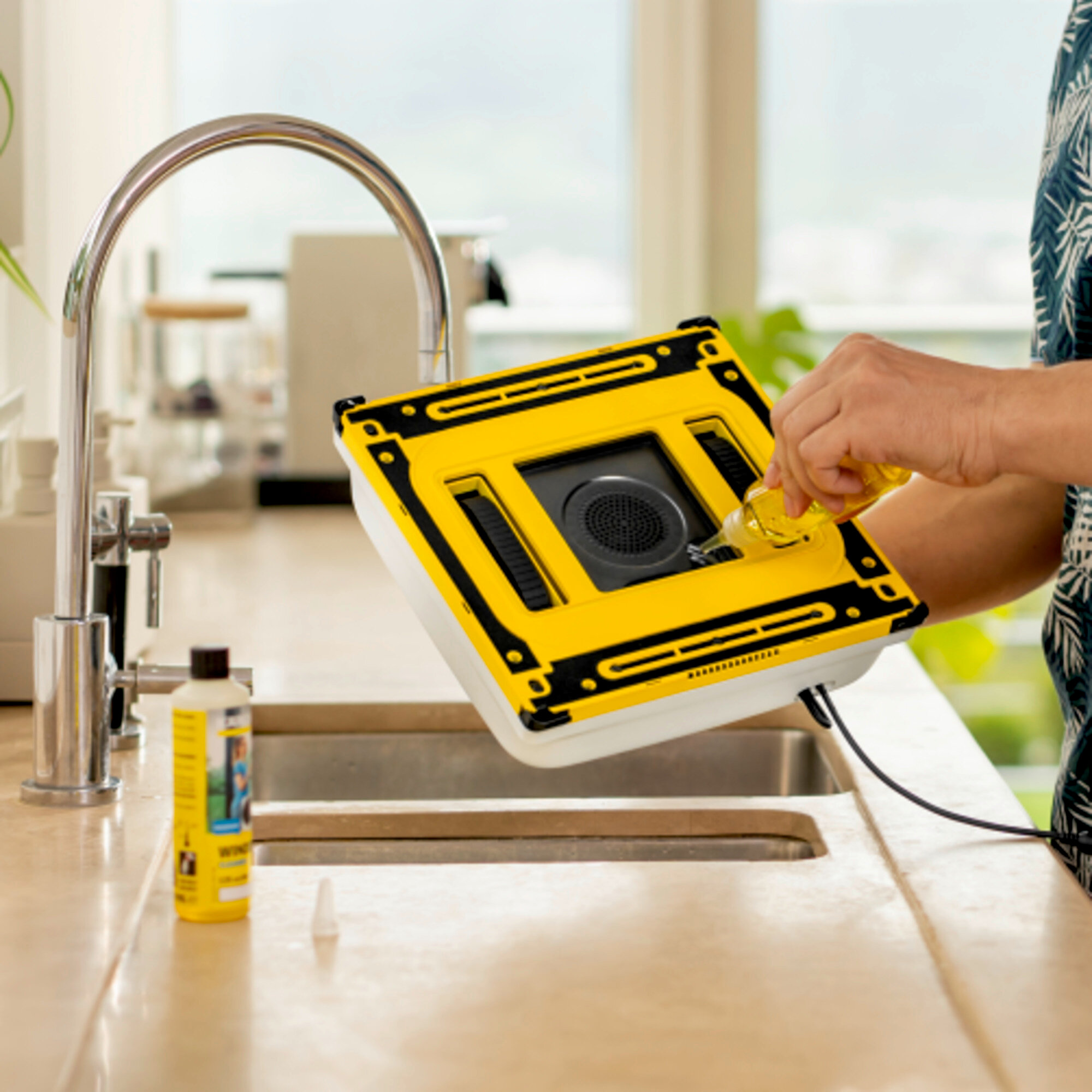 Un robot pulitore giallo viene riempito di liquido dalla mano di una persona vicino a un lavello.