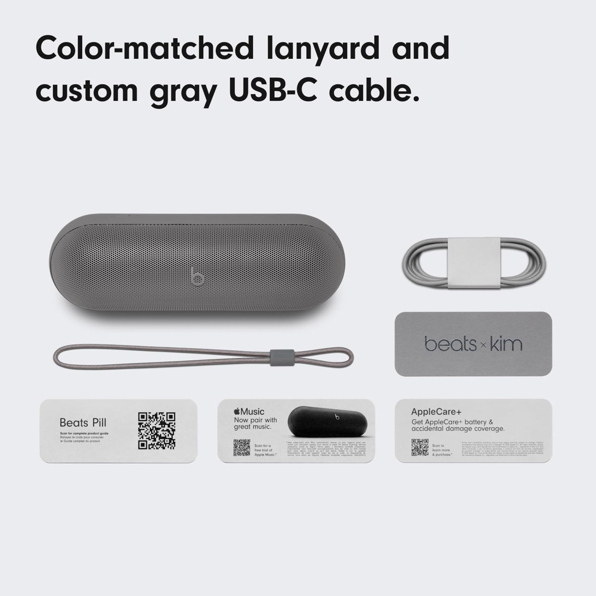 Grauer Beats Pill Lautsprecher mit passendem Lanyard und USB-C-Kabel.