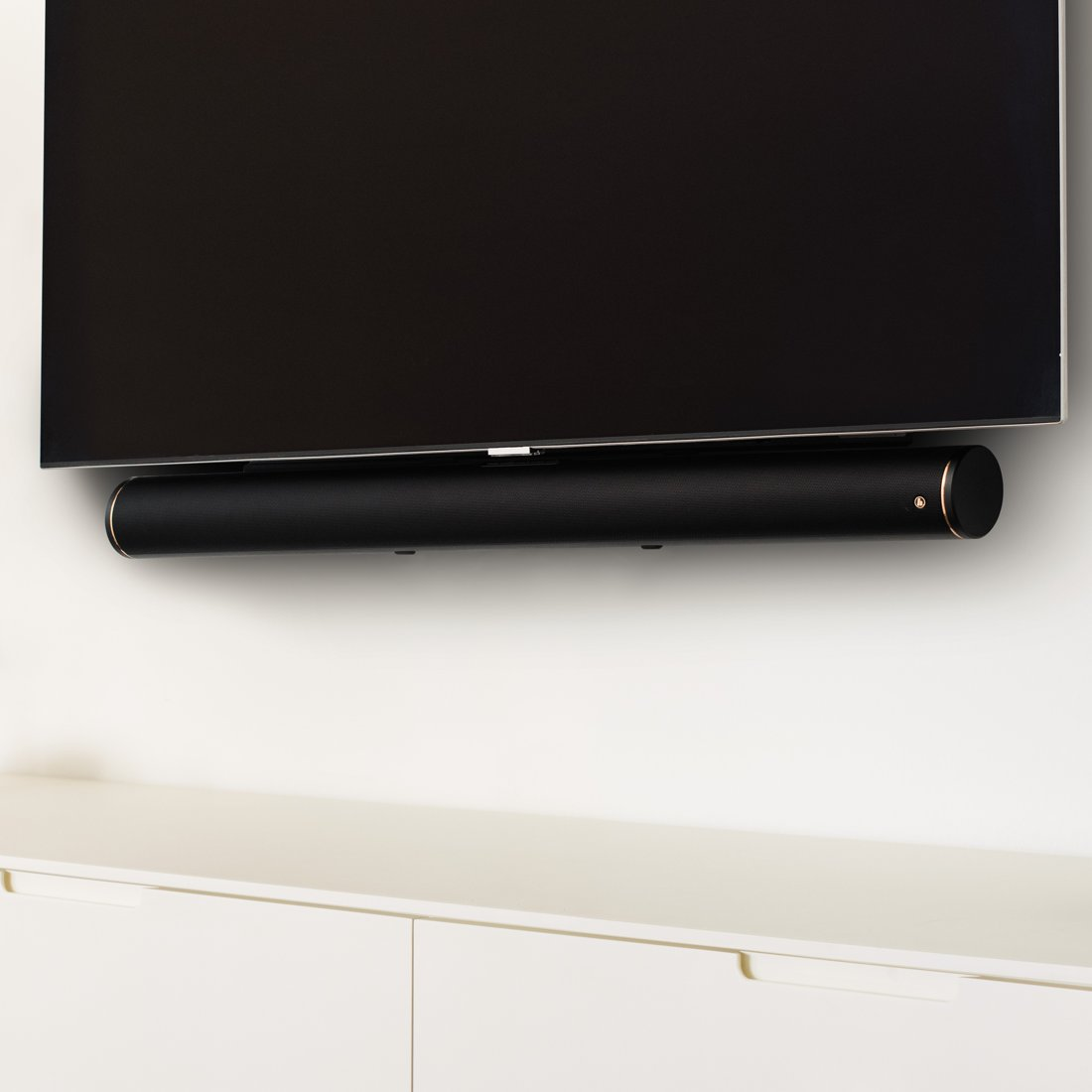 Czarny soundbar pod telewizorem, zamontowany na białej ścianie.