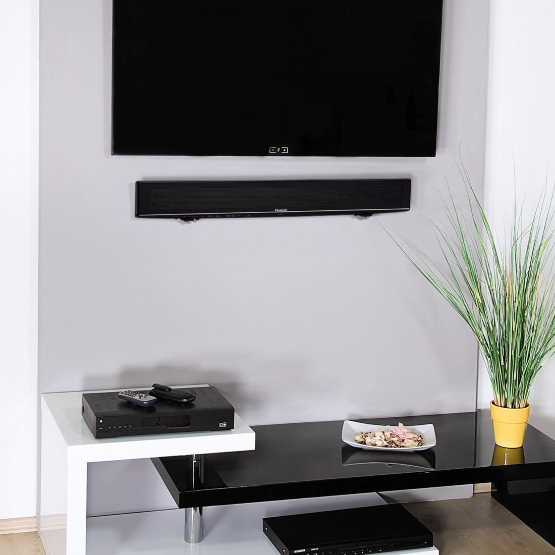 Telewizor płaskoekranowy nad czarną listwą dźwiękową na ścianie, obok odbiornik.
