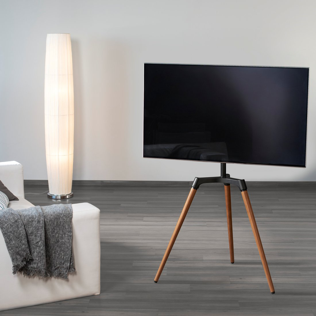 Nowoczesny telewizor stoi na statywie obok białej sofy z kocem.