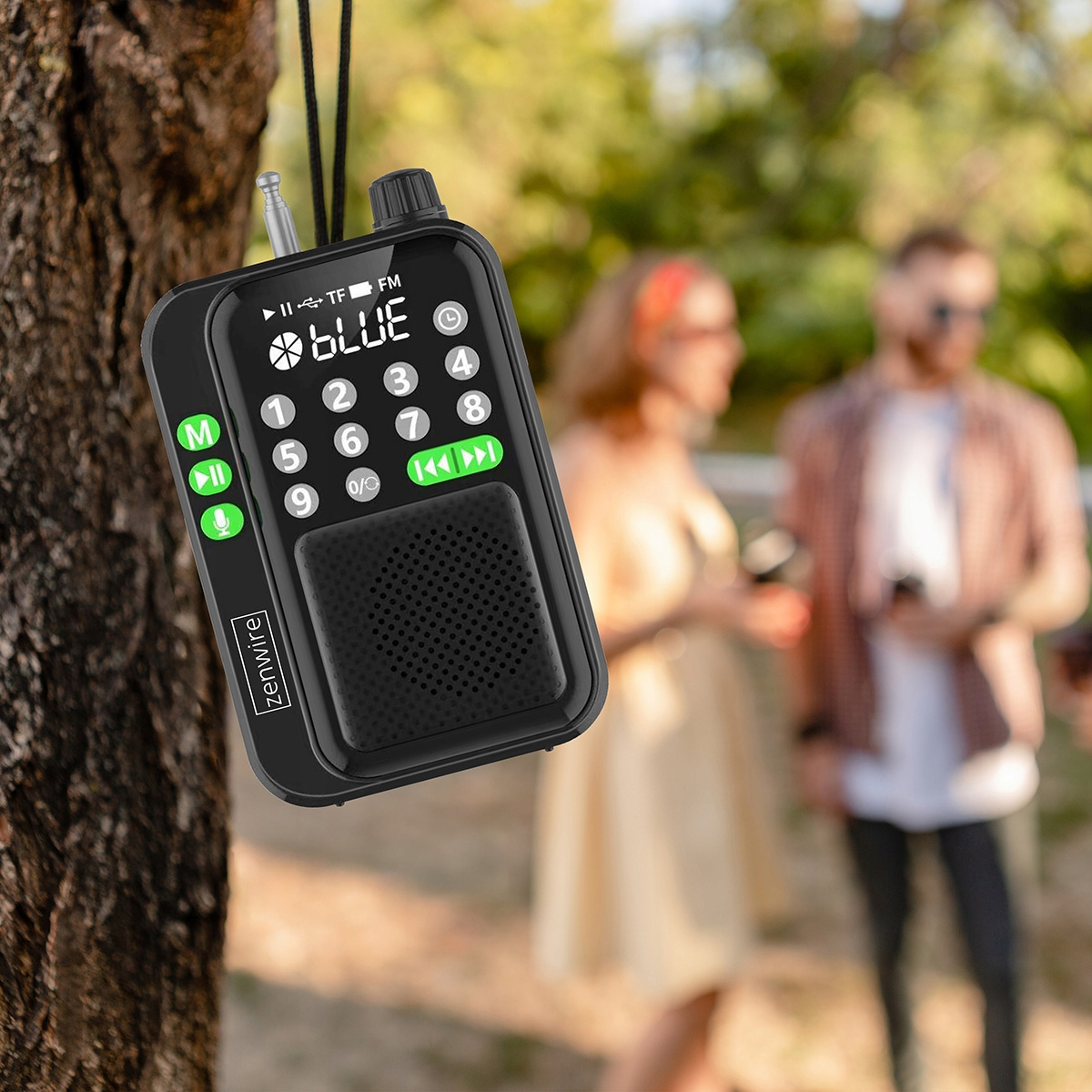 Czarny radiofon wisi na drzewie, ludzie w tle.