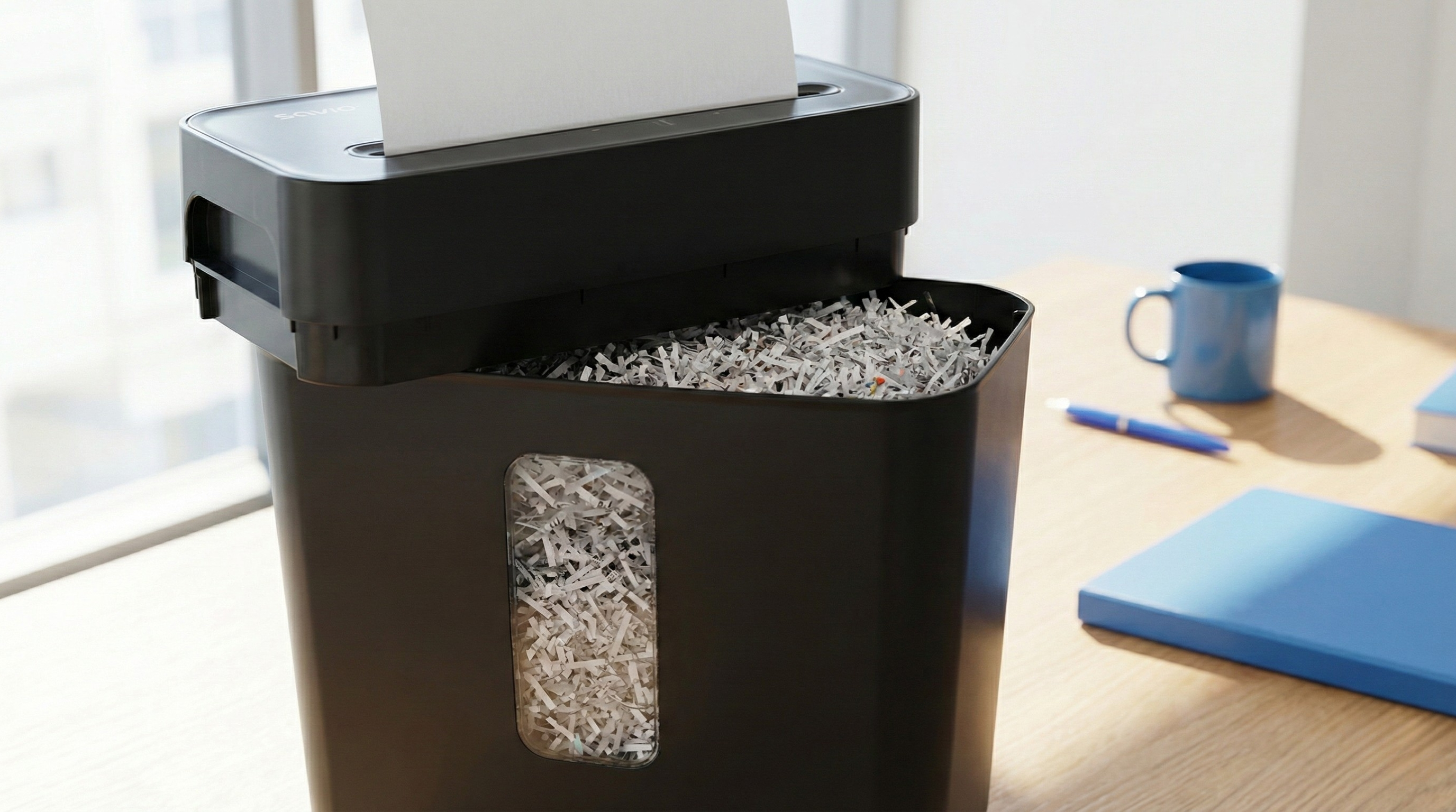 Czarna niszczarka do papieru na drewnianym biurku z posiekanym papierem.