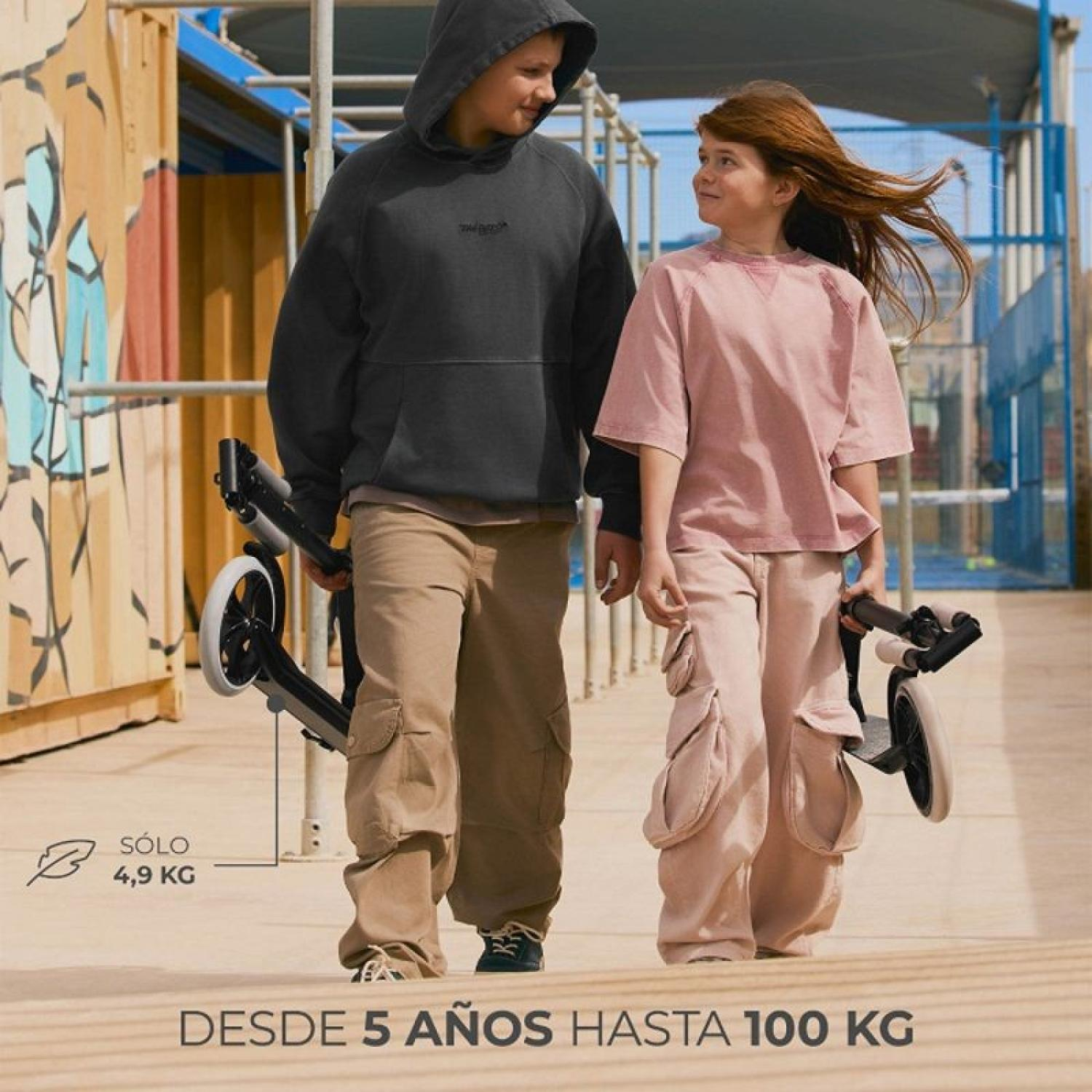 Zwei Kinder gehen mit Rollern. Der Junge trägt einen schwarzen Hoodie, das Mädchen ein rosa T-Shirt.