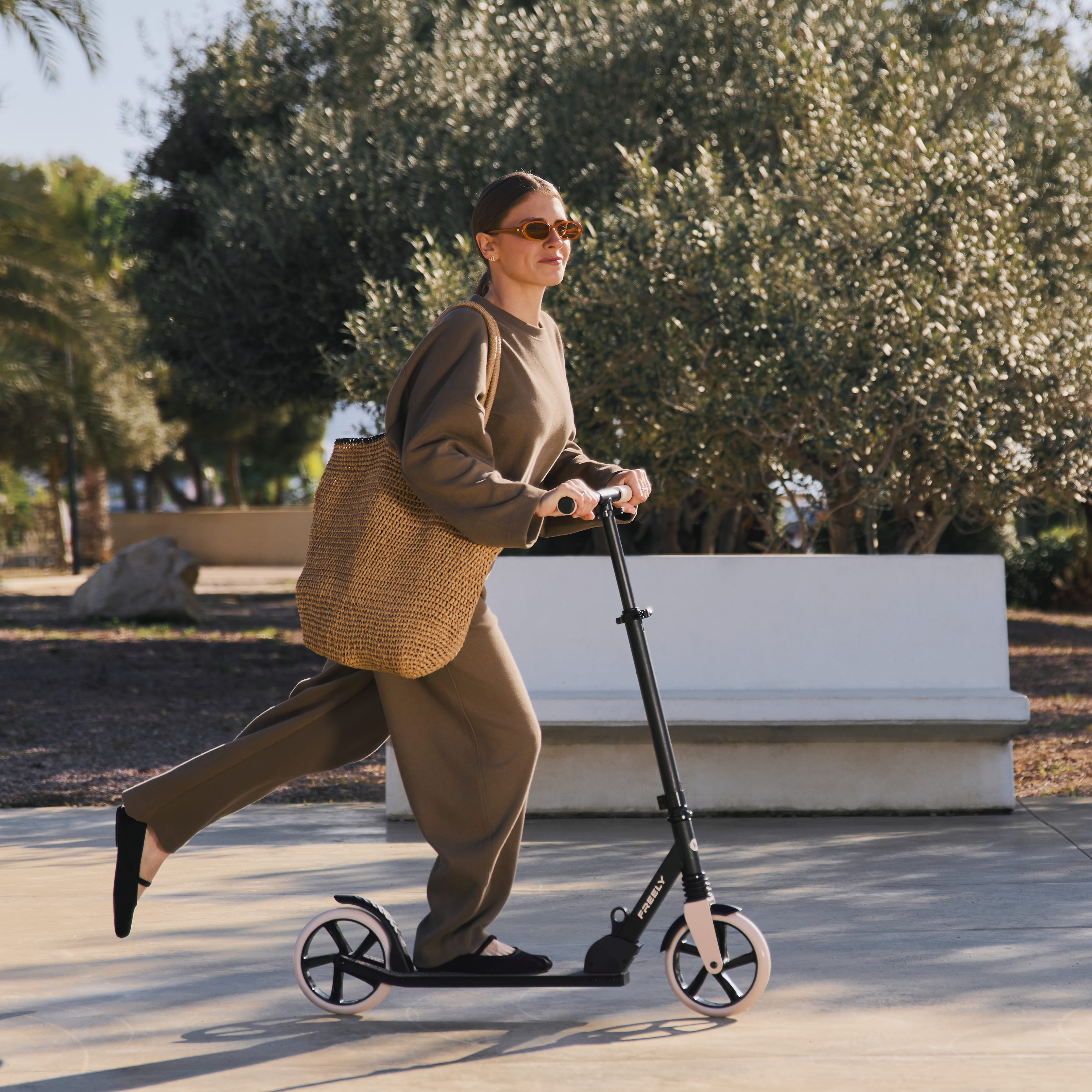 Eine Frau fährt einen Roller in einer grünen Uniform, trägt eine Tasche und Sonnenbrille.