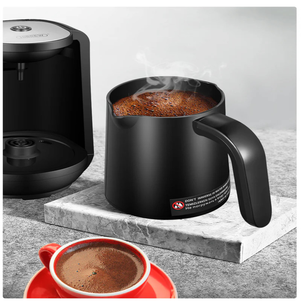 Ein schwarzer Kaffeekocher mit dampfendem Kaffee, daneben eine rote Tasse.