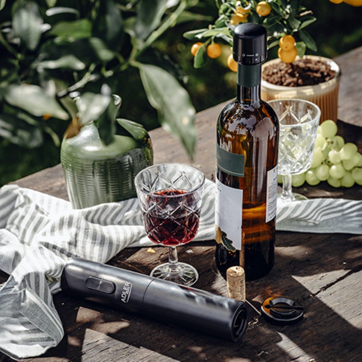 Wein, Gläser und Korkenzieher auf Holztisch im Garten.