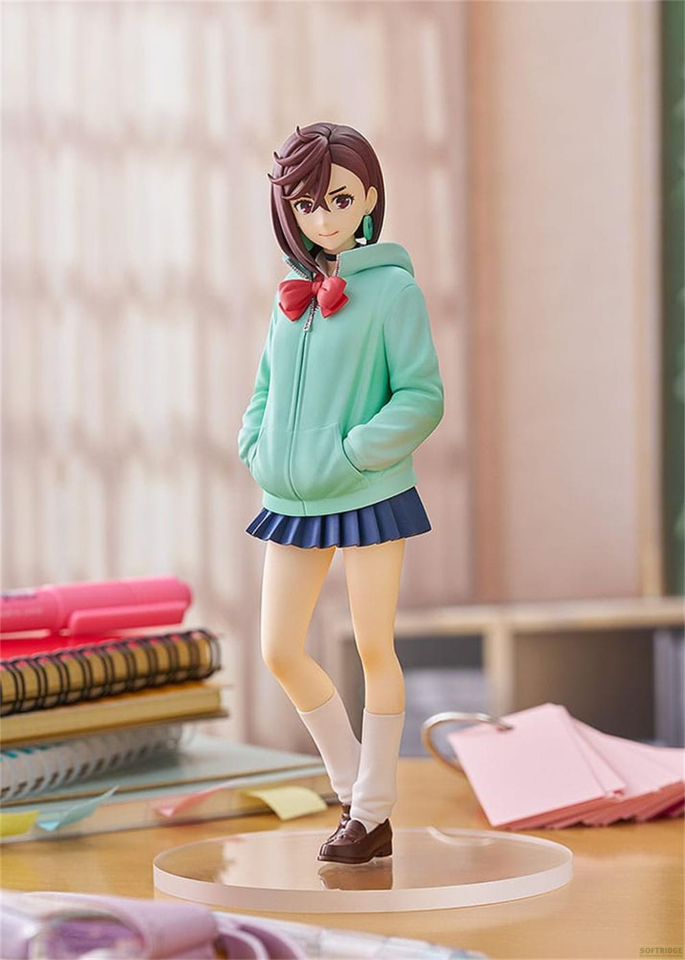 Figura de chica con sudadera verde menta y falda plisada azul sobre un escritorio.
