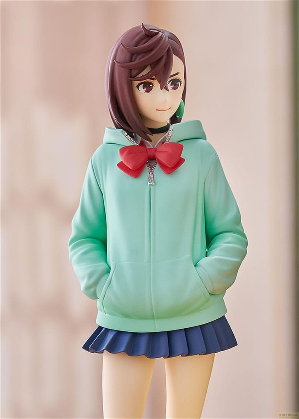 Una figura con sudadera verde claro, lazo rojo y falda plisada azul.