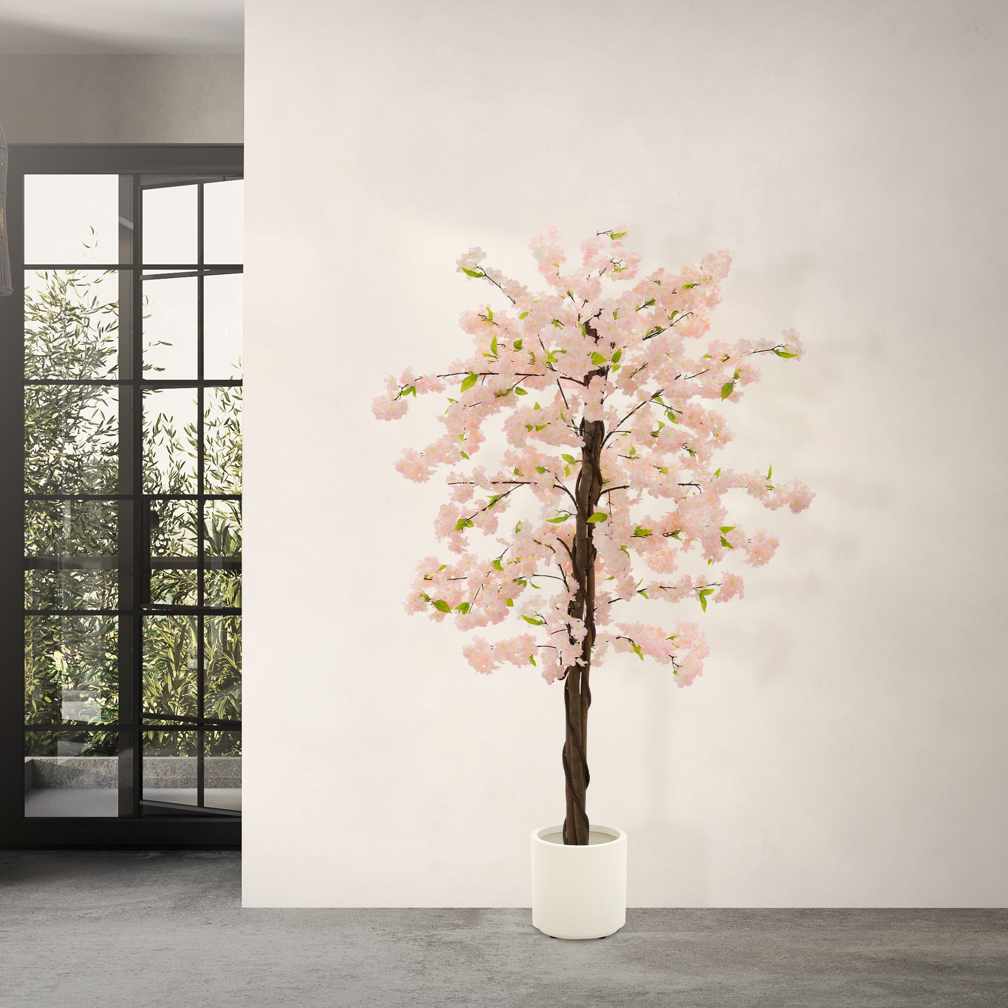 Ein künstlicher Kirschbaum mit rosa Blüten steht in einem weißen Topf auf Betonboden.