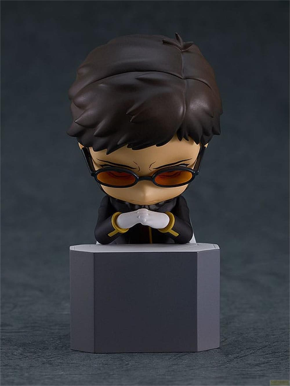 Una figura chibi con pelo oscuro, gafas y traje negro se sienta sobre una base gris.