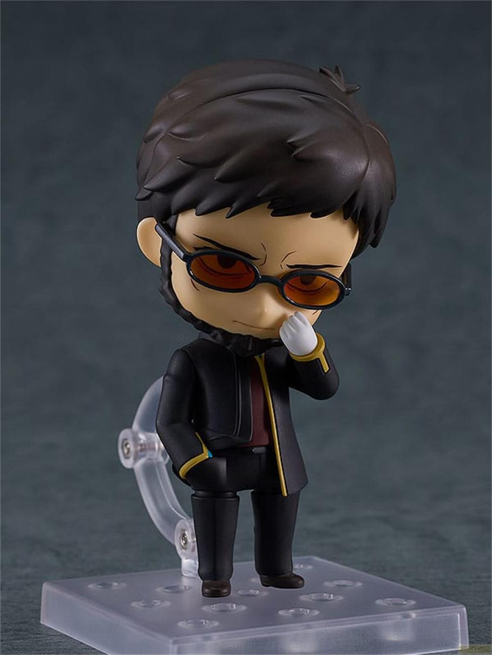 Una figura chibi con pelo castaño, gafas y traje negro.