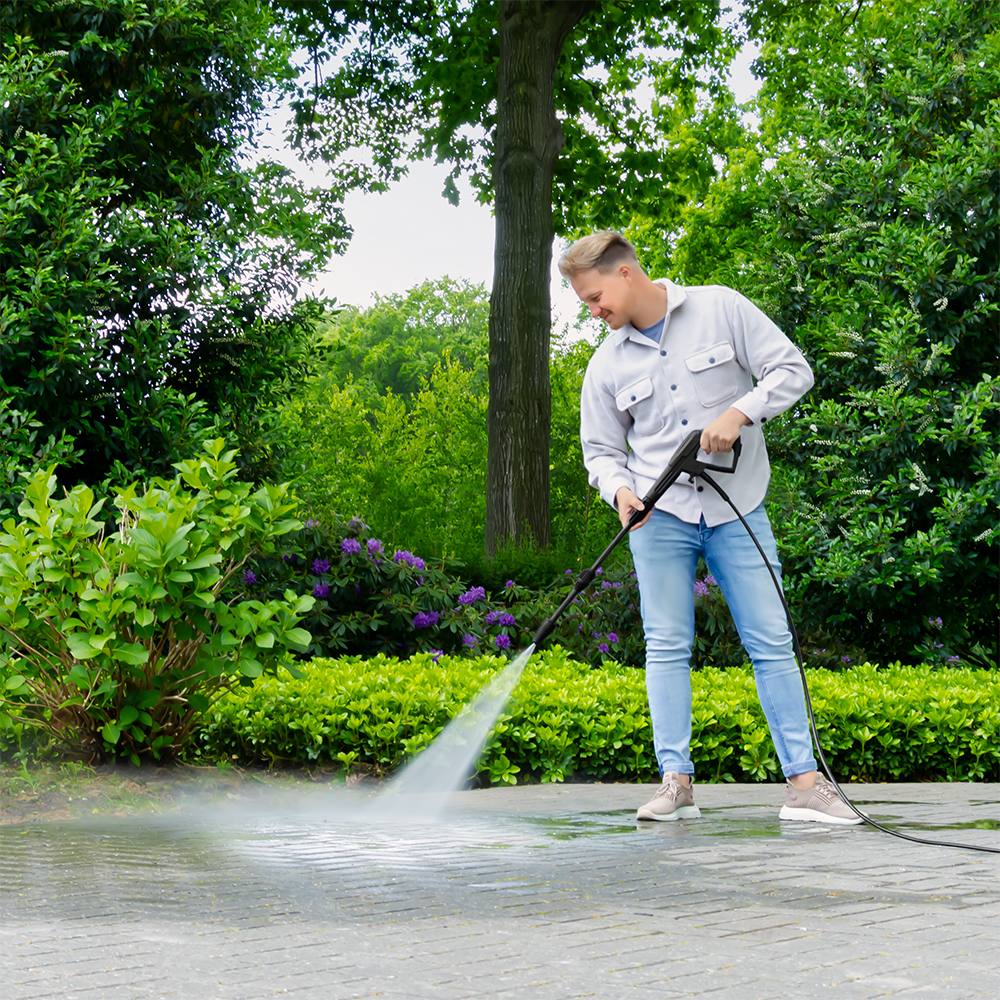 Man reinigt bestrating met hogedrukreiniger in een tuin.