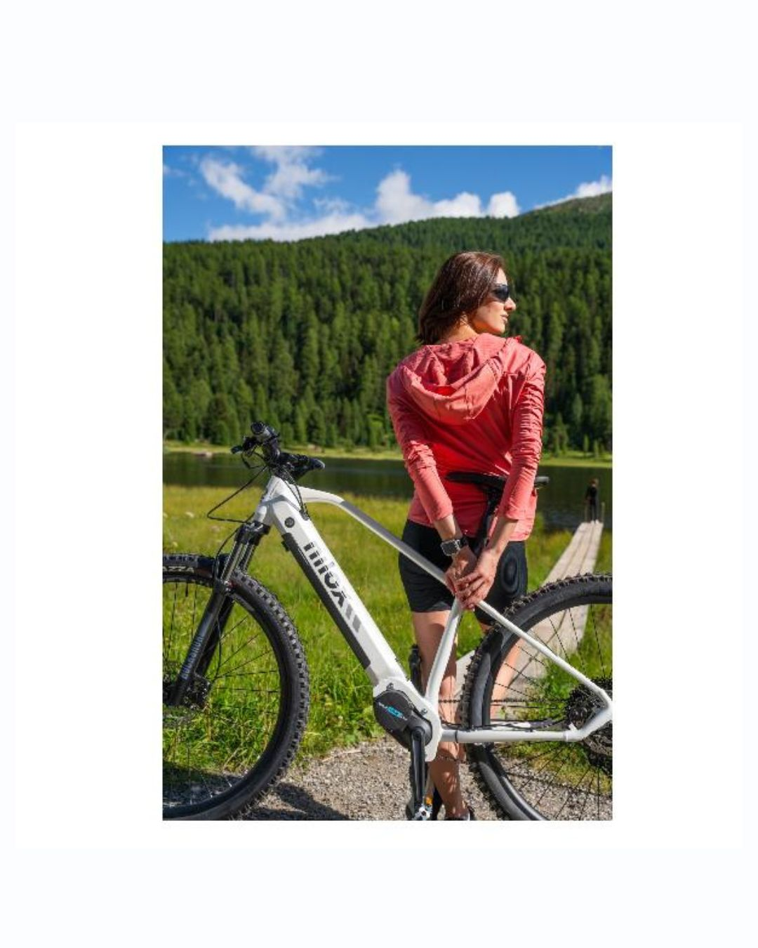 Donna con e-bike all'aperto vicino a foresta e lago, giornata soleggiata.