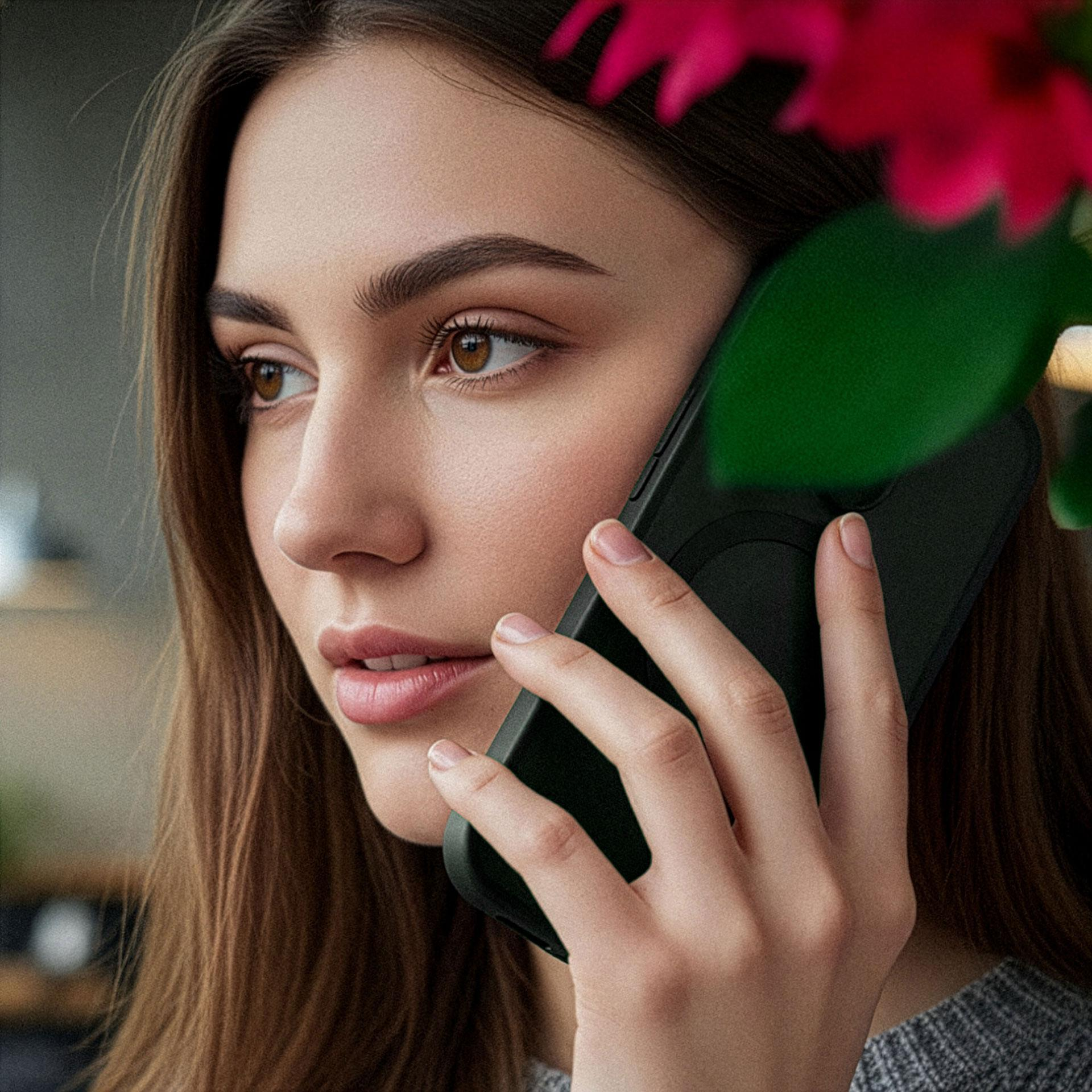 Kobieta z brązowymi włosami rozmawia przez telefon, w pobliżu czerwone płatki i zielone liście.